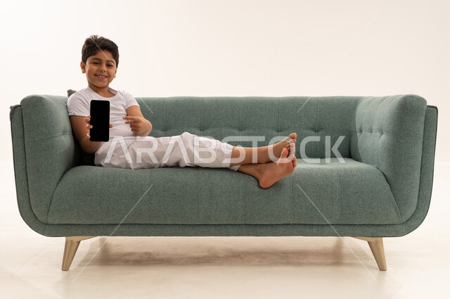 طفل سعودي يحمل هاتف ذكي بشاشة فارغة على الأريكة