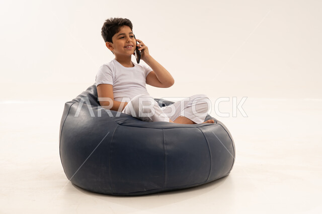 طفل سعودي يتحدث بالهاتف جالساً على كرسي محشو