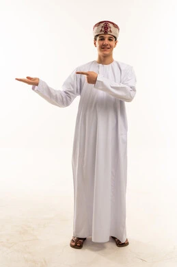 ولد عُماني بالدشداشة يشير بيده على خلفية بيضاء