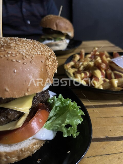 صورة مقربة لساندويش الهمبرجر اللذيذ المحشو باللحم والجبن مع الطماطم والخس ، طلب وجبة البرجر في المطعم ، تقديم وجبات طعام سريعة ، مطاعم عربية