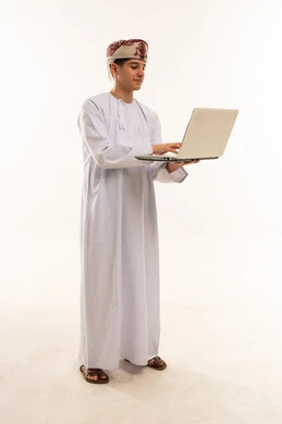 رجل عماني بالزي التقليدي يستخدم الحاسوب المحمول