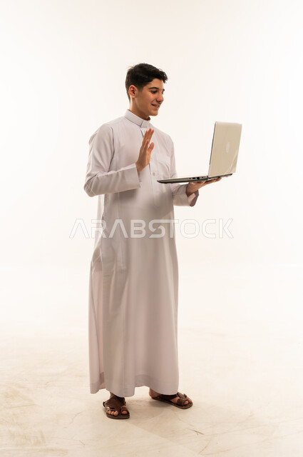 شاب سعودي بالثوب يستخدم لابتوب على خلفية بيضاء