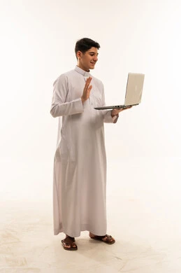 شاب سعودي بالثوب يستخدم لابتوب على خلفية بيضاء