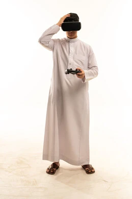 رجل سعودي يرتدي نظارة واقع افتراضي وجهاز ألعاب