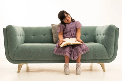 طفلة عربية من ذوي متلازمة داون تقرأ على الأريكة