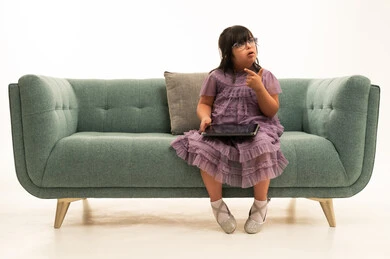 طفلة عربية بمتلازمة داون تستخدم جهازاً لوحياً على الأريكة