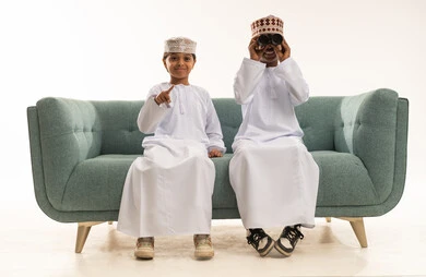 Omani Boys in Traditional Dress with Binoculars on Sofa