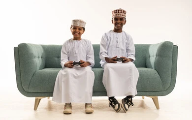 أطفال عمانيون يلعبون بالزي التقليدي على أريكة زرقاء