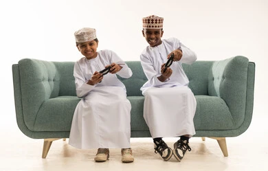 أطفال عمانيون يلعبون ألعاب الفيديو على أريكة