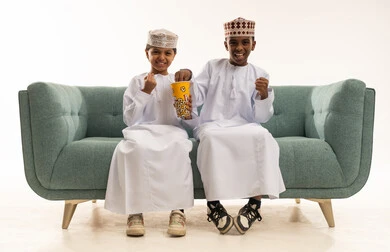 Omani Boys Eating Popcorn on Sofa in Traditional Dress
