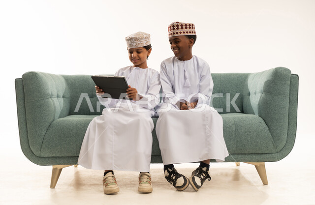 Omani Boys in Traditional Dress Using Tablet on Sofa