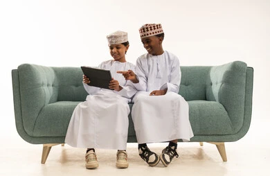 Omani Boys in Traditional Dress Using Tablet on Sofa