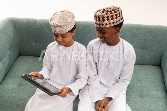 أطفال عمانيون بالزي التقليدي يستخدمون جهازاً لوحياً