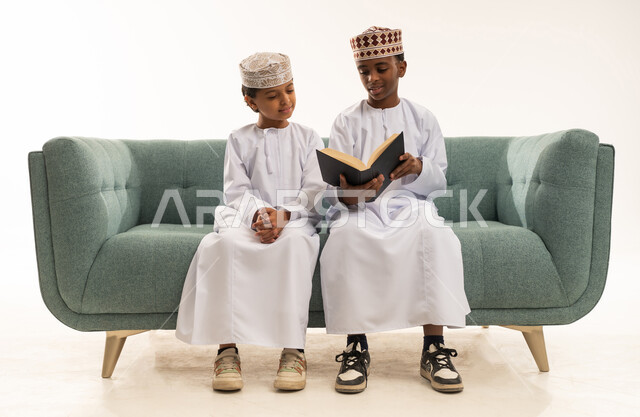 أطفال عمانيون بالزي التقليدي يقرأون على الأريكة