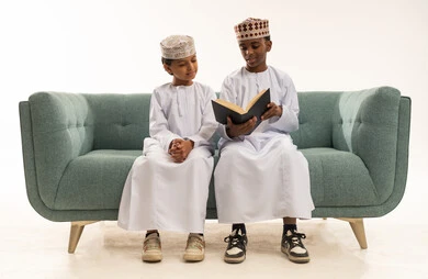 أطفال عمانيون بالزي التقليدي يقرأون على الأريكة