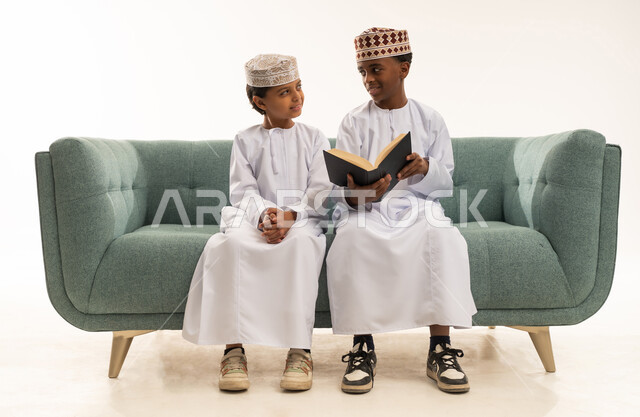 أطفال عمانيون باللباس التقليدي يقرؤون على الأريكة