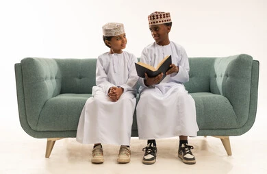 أطفال عمانيون باللباس التقليدي يقرؤون على الأريكة