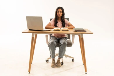 طالبة سعودية تجلس على مكتب مع كمبيوتر محمول وكتب