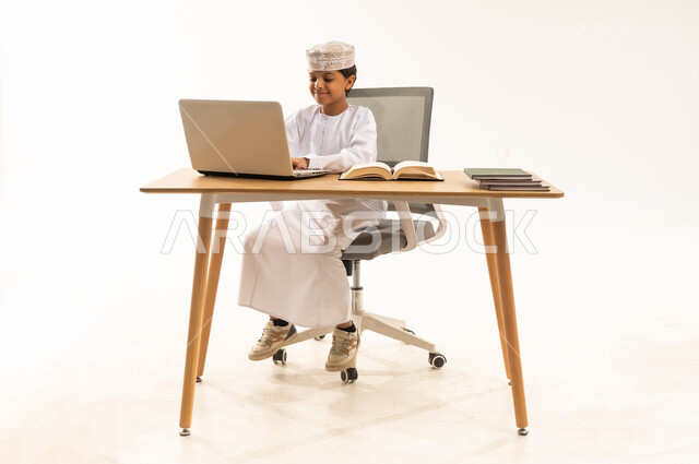 طفل عماني يستخدم الحاسوب المحمول على مكتب في استوديو