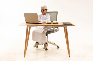 طفل عماني يستخدم الحاسوب المحمول على مكتب في استوديو