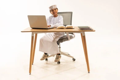 طفل عُماني يدرس باستخدام الحاسوب أمام خلفية بيضاء