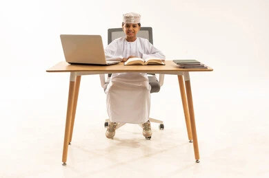 طالب عماني مع حاسوب محمول وكتب دراسية