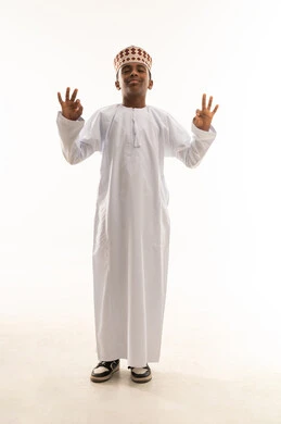 طفل عماني بالزي التقليدي يقوم بإيماءة الرضا والنجاح