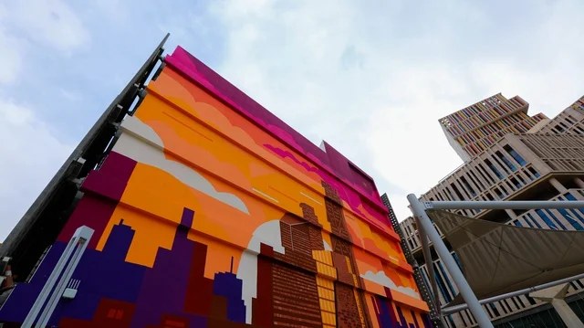 واجهة مبنى حديث  بجدارية فنية معاصرة ، ألوان دافئة وحيوية، تجسّيد أفق المدينة بأسلوب هندسي مبسّط، الأشكال المعمارية الفنية، الإبداع الحضري والتطور المعماري في المملكة العربية السعودية .