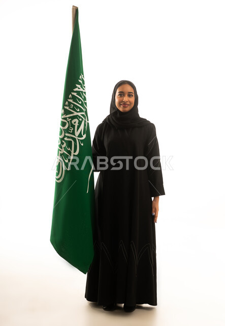 امرأة سعودية تقف بجانب العلم الوطني بخلفية بيضاء