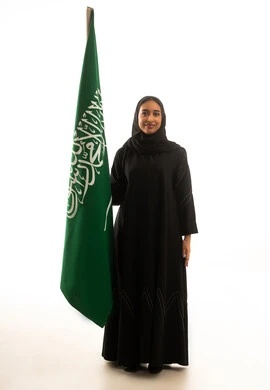 امرأة سعودية تقف بجانب العلم الوطني بخلفية بيضاء