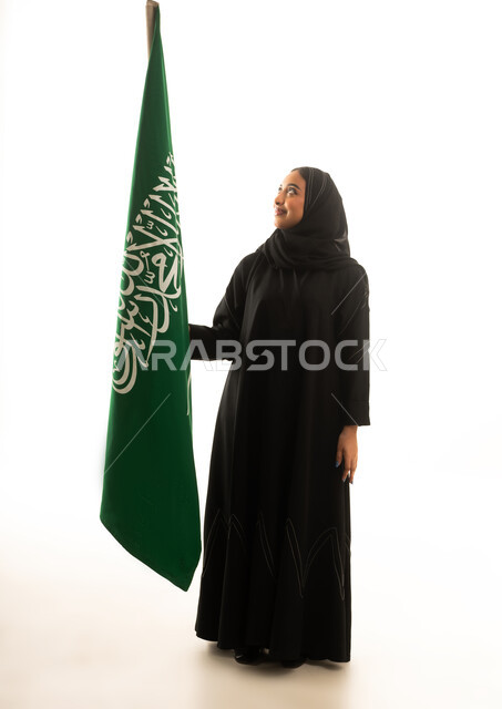 امرأة سعودية بالعباءة تقف مع العلم السعودي