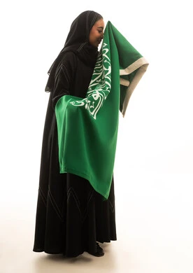 امرأة سعودية بالعباءة تحمل العلم السعودي