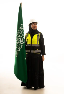مهندسة سعودية مع العلم الوطني وسترة السلامة