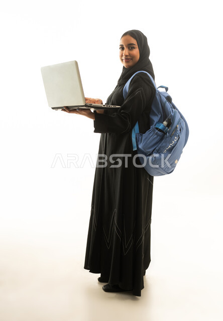 امرأة سعودية تحمل حاسوباً محمولاً وحقيبة ظهر بخلفية بيضاء