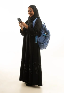 طالبة سعودية بعباءة تحمل هاتف وحقيبة ظهر