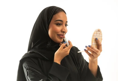 امرأة سعودية تضع أحمر الشفاه أمام المرآة بخلفية بيضاء