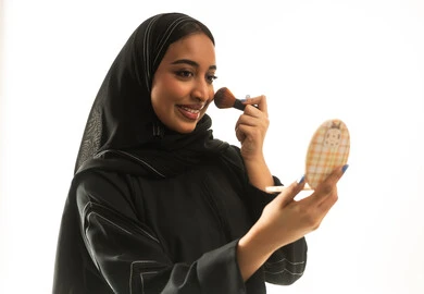 Saudi Woman Applying Makeup with Brush on White Background