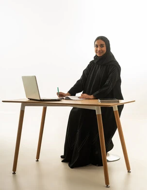 امرأة سعودية مع كمبيوتر محمول على مكتب خلفية بيضاء