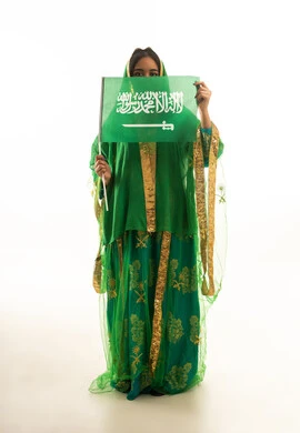 امرأة سعودية تحمل العلم بالزي التقليدي الأخضر