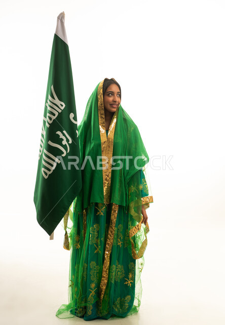 امرأة سعودية بالزي التقليدي مع علم المملكة العربية السعودية