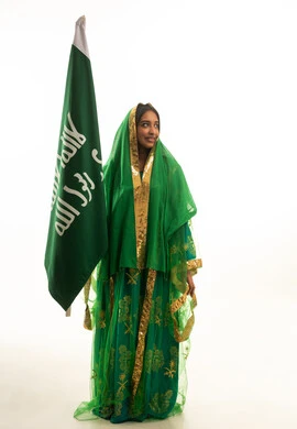 امرأة سعودية بالزي التقليدي مع علم المملكة العربية السعودية