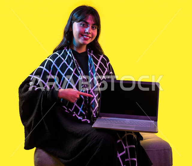 بورتريه لمرأة خليجية سعودية ، إستخدام جهاز الحاسوب المحمول ، عرض شاشة اللابتوب ، إستخدام أجهزة تقنية حديثة ، جلسة عمل ، تصفح الإنترنت ، عرض خدمات وتطبيقات عبر اللابتوب، التسويق الرقمي الإلكتروني ، مفهوم الإعلانات، خلفية صفراء
