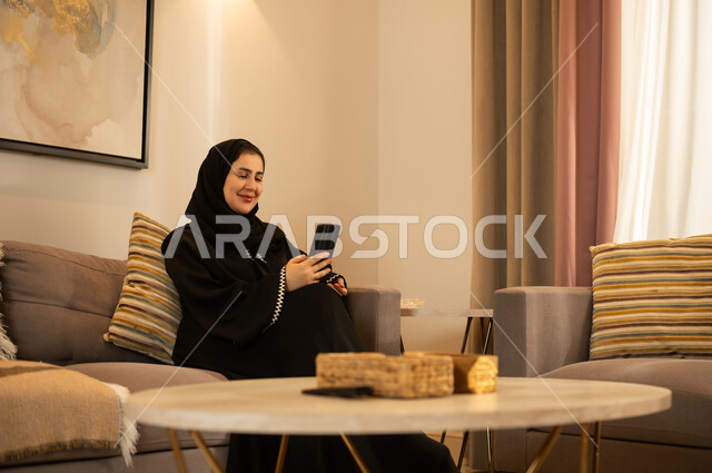 امرأة سعودية مع هاتف ذكي في غرفة معيشة حديثة