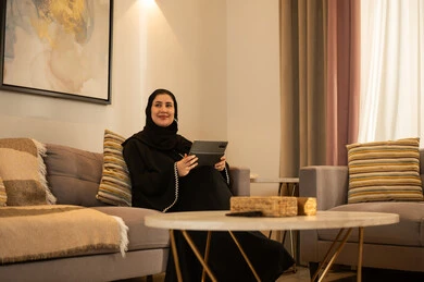 امرأة سعودية مع جهاز لوحي في غرفة معيشة حديثة