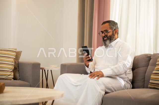 رجل سعودي يستخدم الهاتف الذكي في غرفة معيشة حديثة