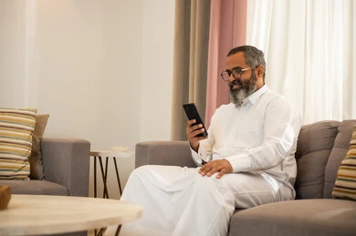 رجل سعودي يستخدم الهاتف الذكي في غرفة معيشة حديثة