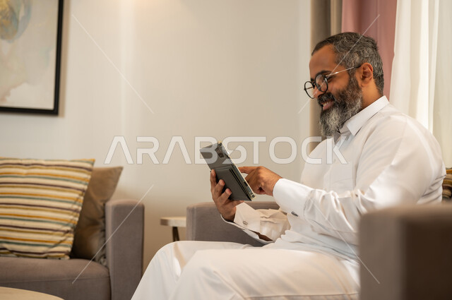 رجل سعودي بالثوب يستخدم جهاز لوحي في المنزل