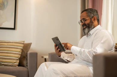 رجل سعودي بالثوب يستخدم جهاز لوحي في المنزل