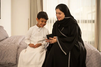 أم سعودية وابنها يستخدمان الهاتف الذكي في غرفة النوم