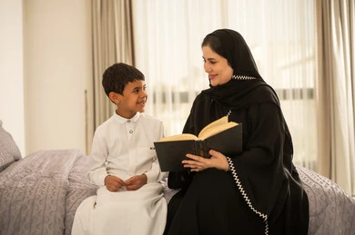 Saudi Mother Reading Book to Son in Bedroom